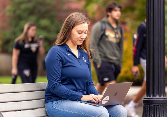student sitting on bench with computer